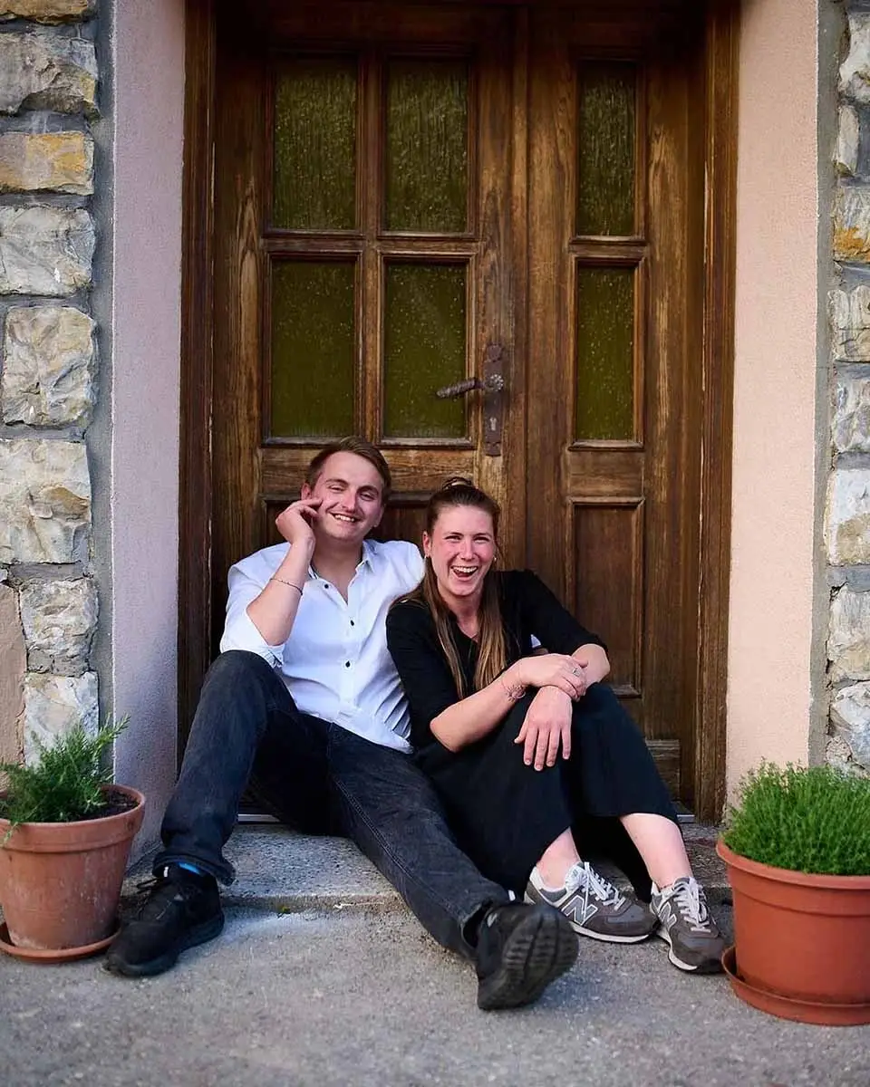 Inhaber Lea Ahammer und Küchenchef Patrick Samek sitzen lachend vor dem Eingang – authentische Gastgeber im 150 Jahre alten Traditionshaus.